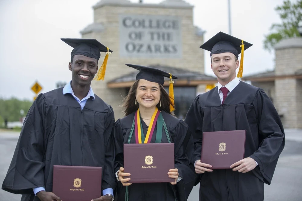 The graduates stand at C of O entrance in full regalia.  